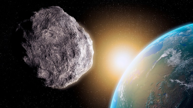 An asteroid floats in space in the foreground, with the Earth in the background.